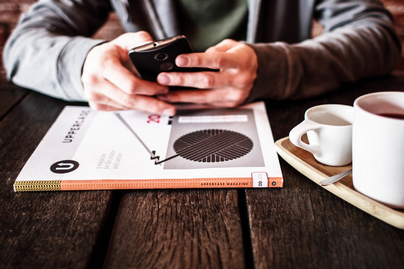 A smartphone lies face up on a wooden table next to a cup of tea and a small plant.